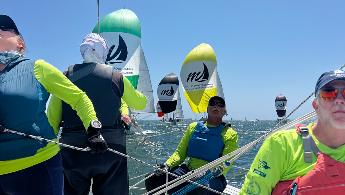 Sailors sailing downwind, flying the spinnaker, ahead of all the other boats