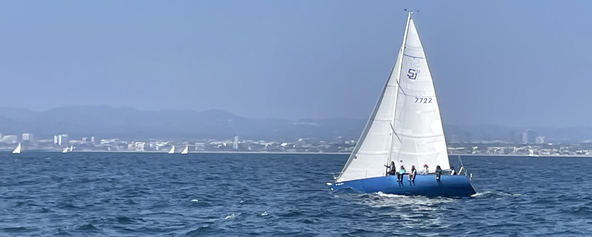 A blue-hulled sailboat, heeled over in the Pacific Ocean for race practice.