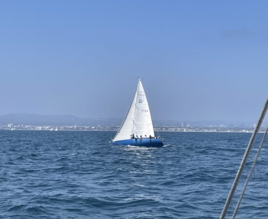 A blue-hulled sailboat, heeled over in the Pacific Ocean for race practice.