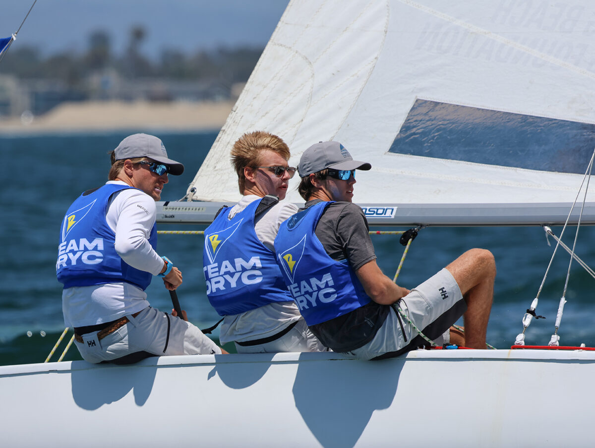 Three young men racing a sailboat, sitting on the rail and headed upwind