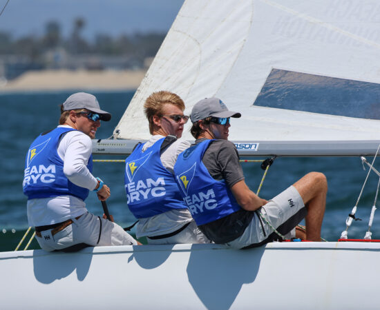 Three young men racing a sailboat, sitting on the rail and headed upwind
